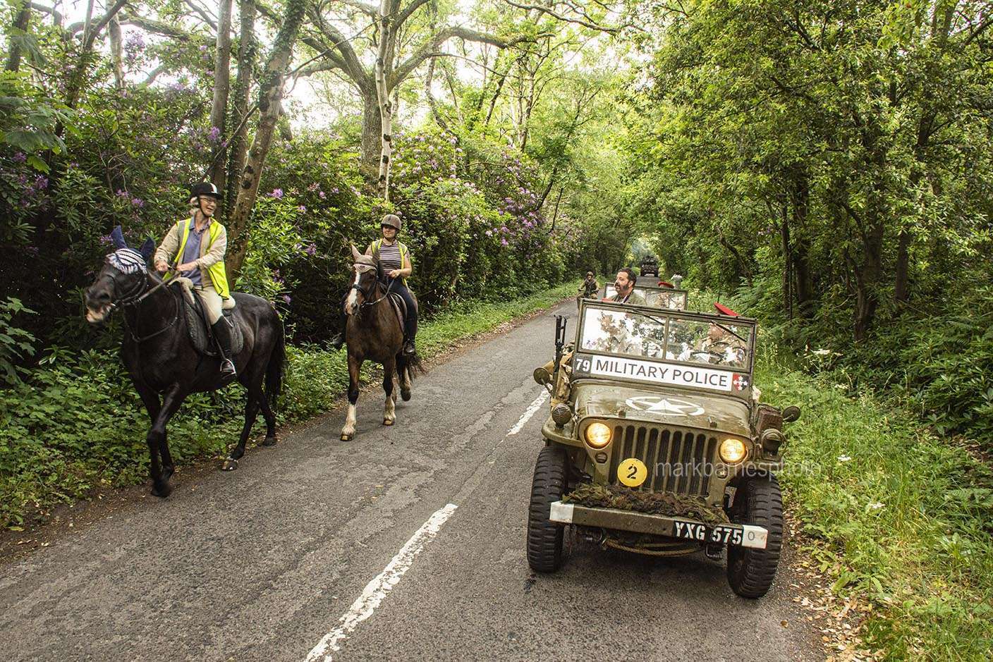 A Jeep carefully passing horse riders.